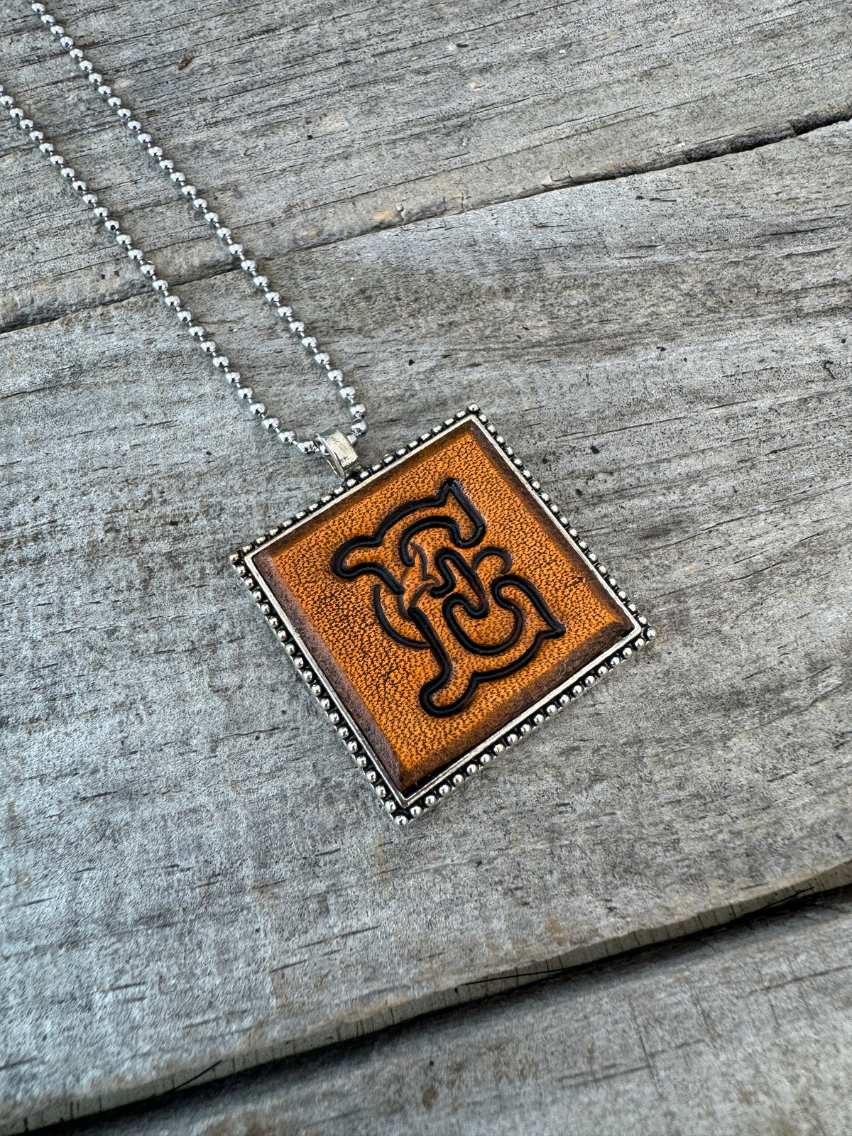 Floral Script letter E hand-stamped leather pendant necklace in a silver-tone square frame