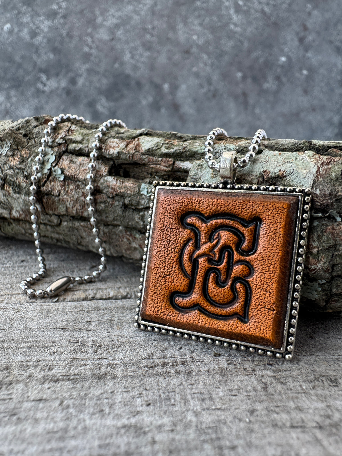 Floral Script letter E leather initial necklace styled on rustic wood with a silver ball chain