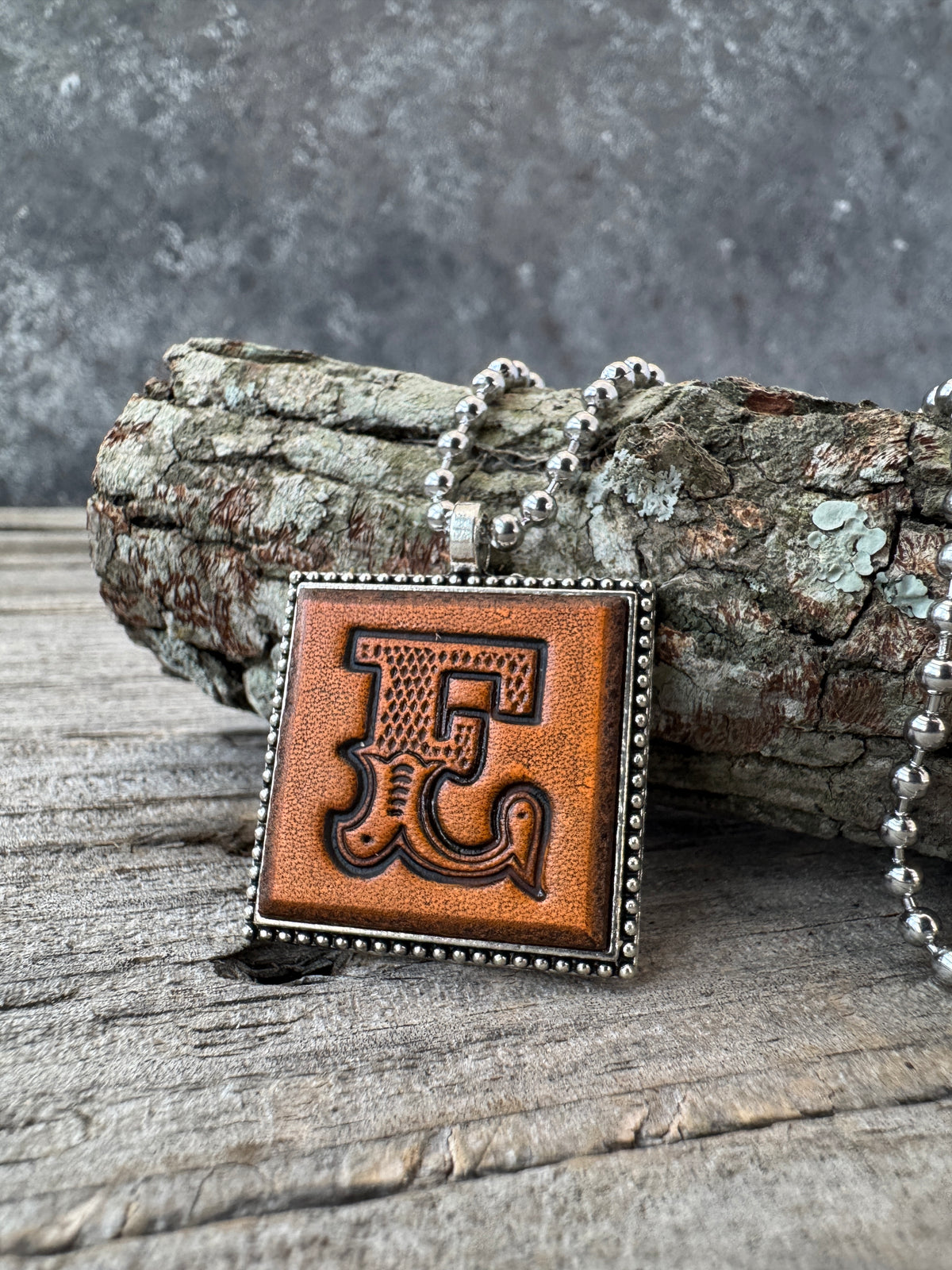 Western Block letter E leather initial necklace styled on rustic wood with a silver ball chain