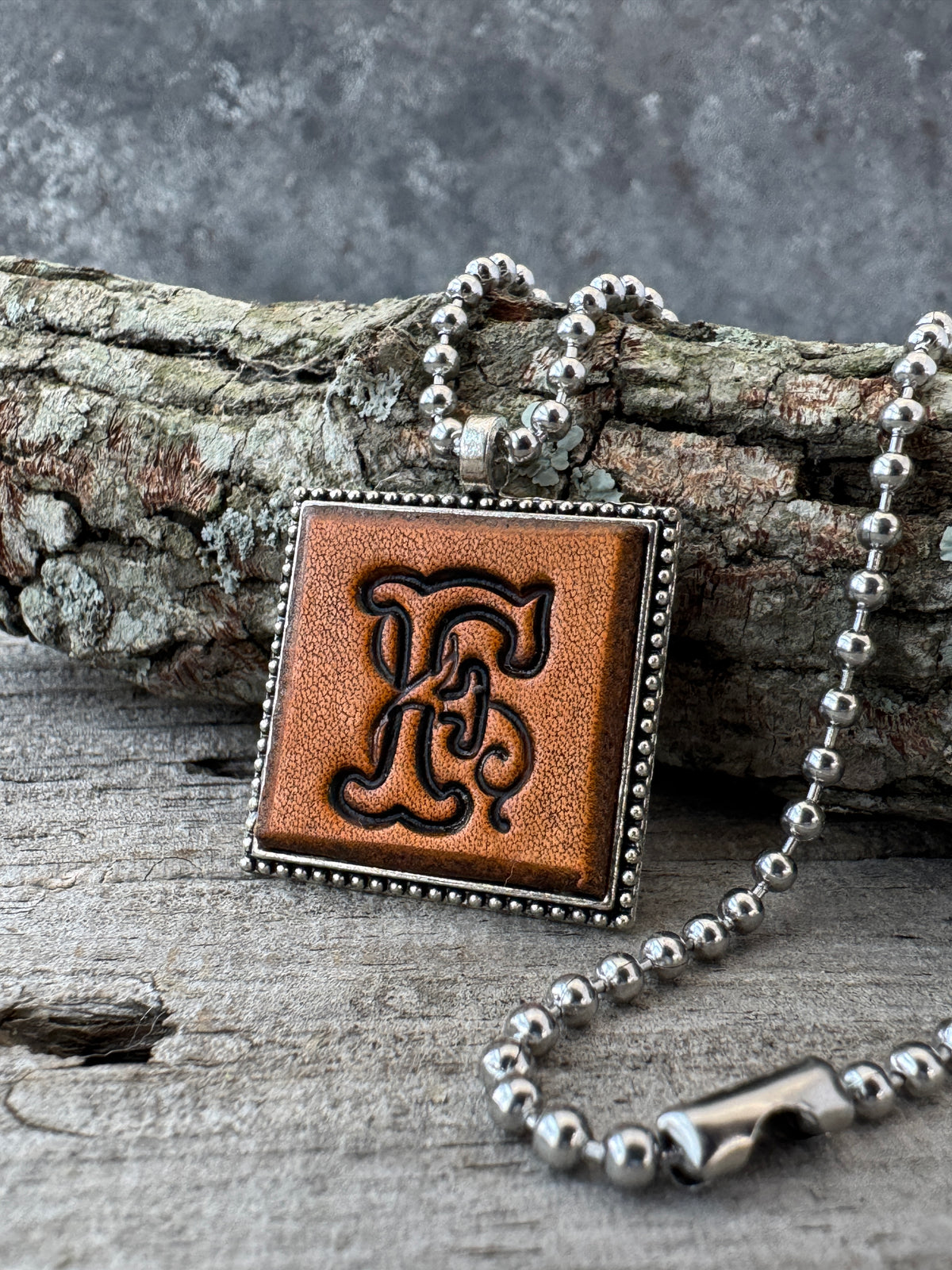 Floral Script letter F leather initial necklace styled on rustic wood with a silver ball chain