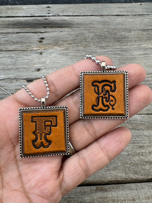 Western Block and Floral Script letter F leather pendants held in hand to show their 1-inch size
