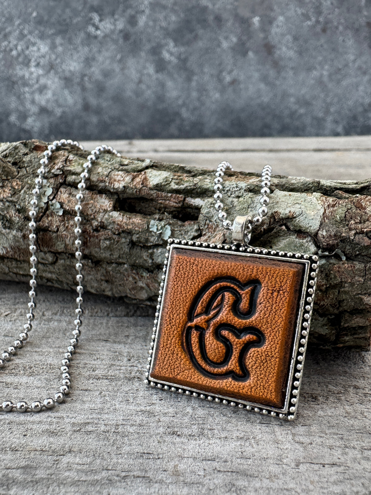 Floral Script letter G leather initial necklace styled on rustic wood with a silver ball chain