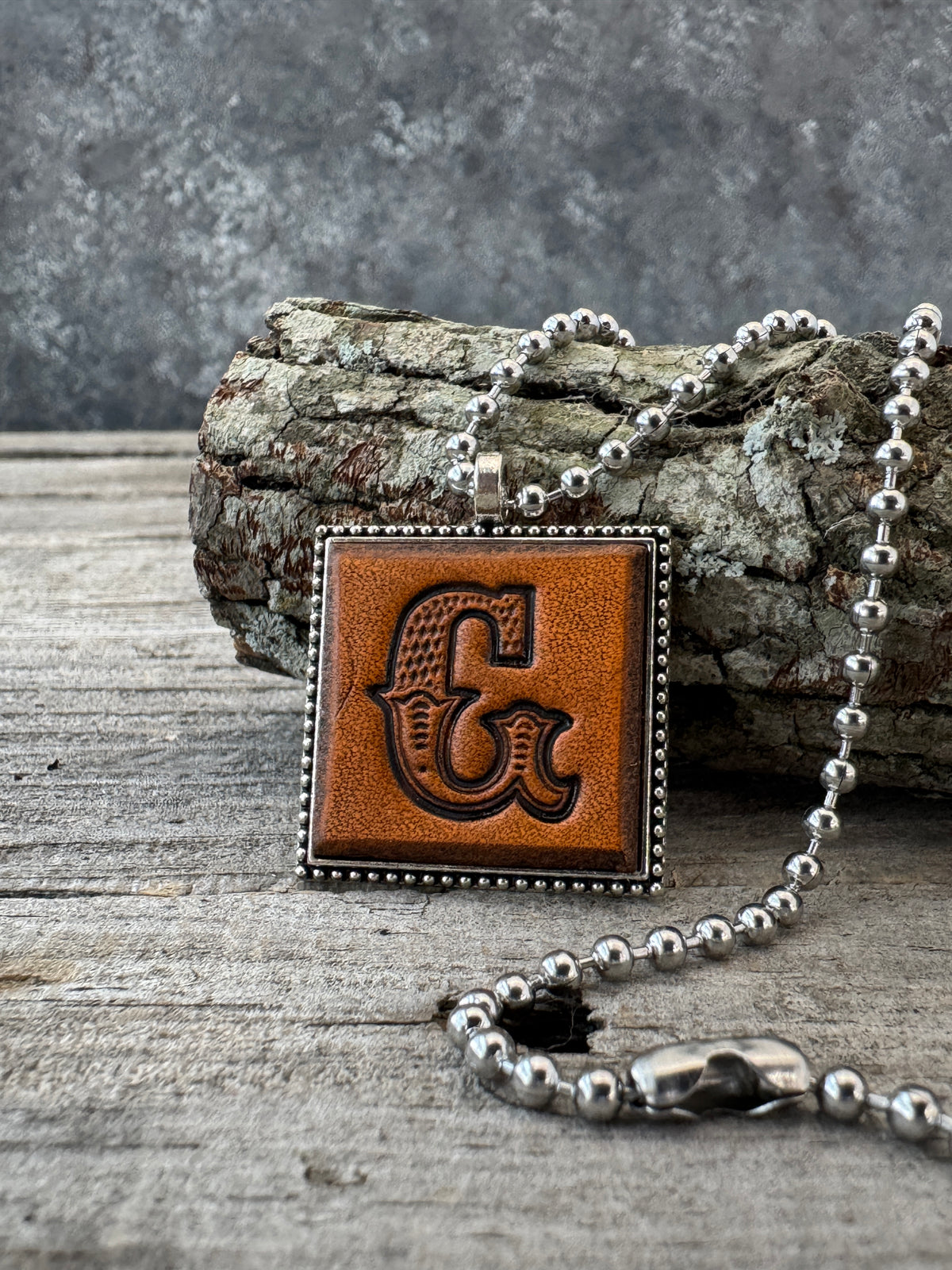 Western Block letter G leather initial necklace styled on rustic wood with a silver ball chain