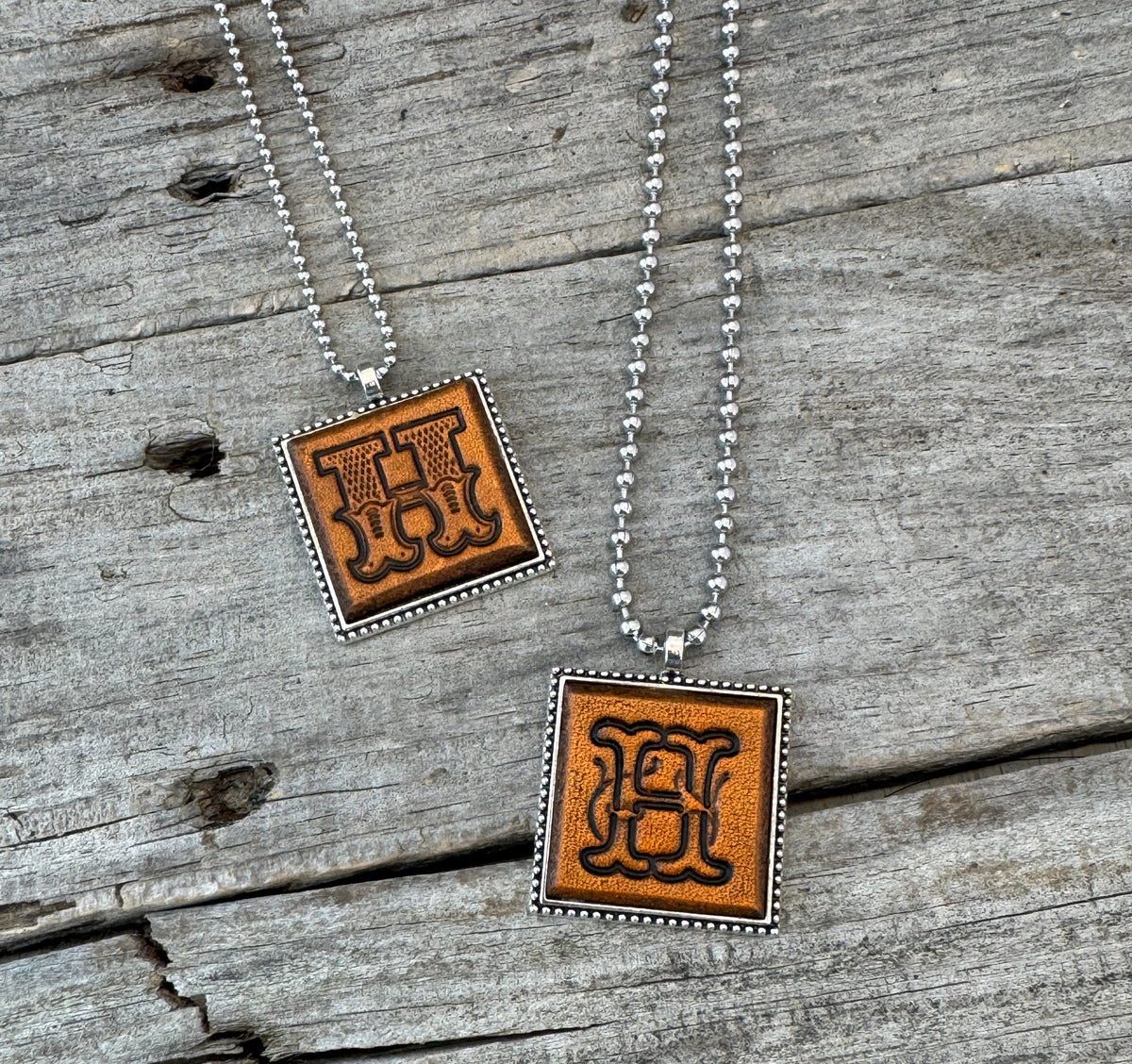 Two handcrafted Letter H leather initial necklaces showing Western Block and Floral Script lettering styles on silver-tone chains.