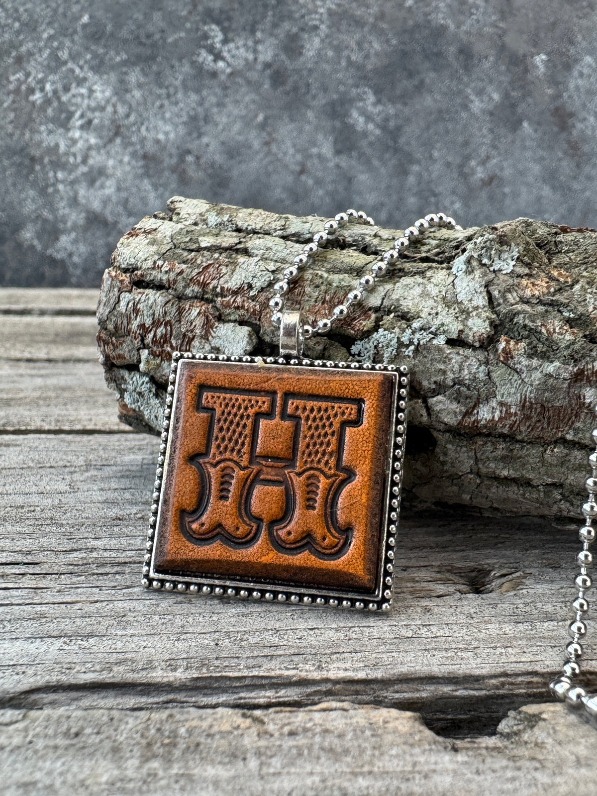 Hand-stamped Western Block Letter H leather necklace with detailed Western lettering displayed against rustic wood and tree bark.