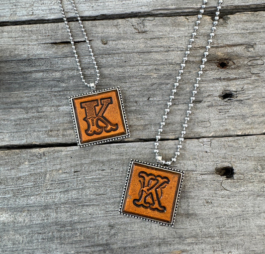 Two handmade Letter K leather initial necklaces showing Western Block and Floral Script lettering styles on genuine brown leather pendants.