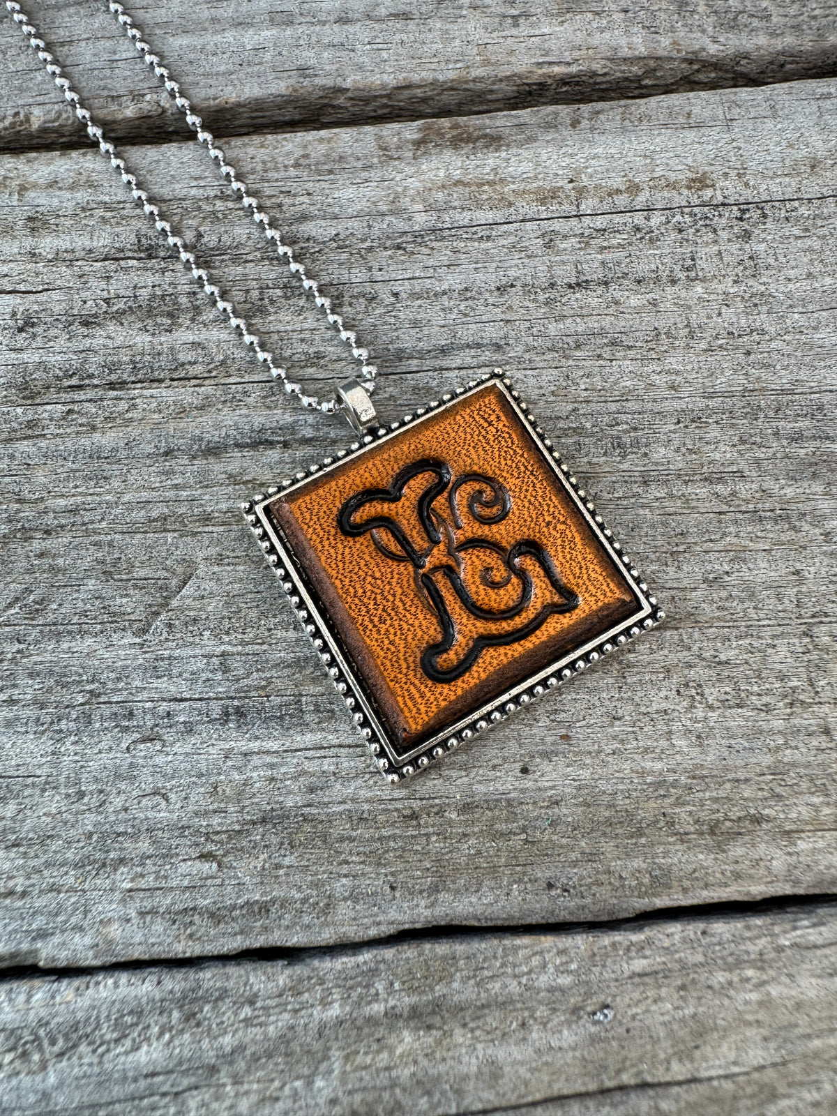 Close-up of hand-stamped Floral Script Letter L leather initial pendant