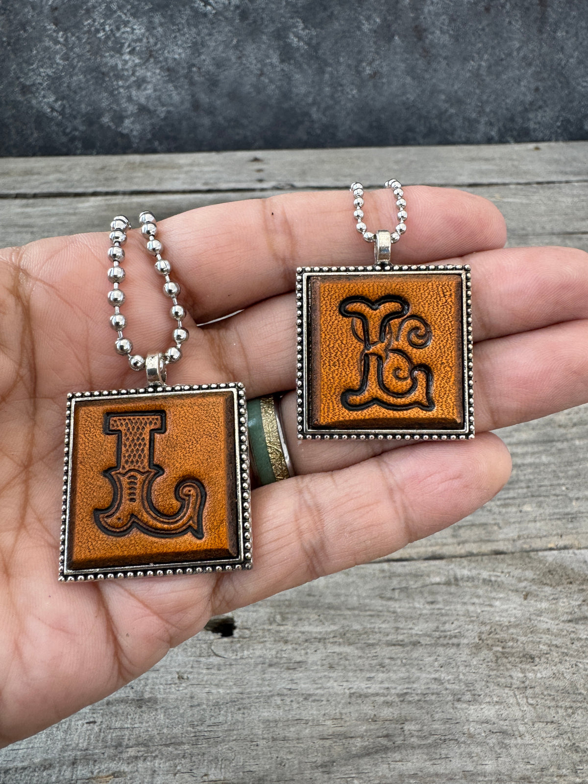 Western Block and Floral Script Letter L leather necklaces held in hand to show pendant size
