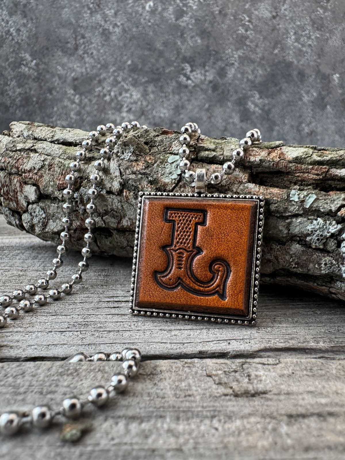Western Block Letter L leather necklace displayed on rustic wood