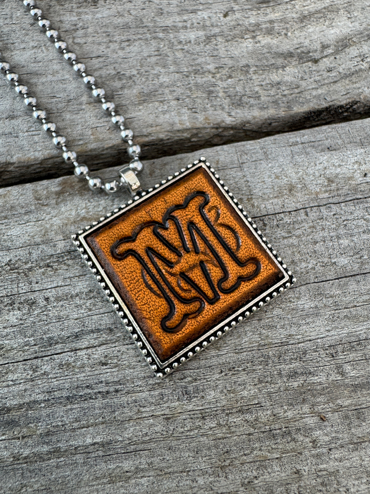 Close-up of Floral Script Letter M leather initial pendant with antiqued lettering