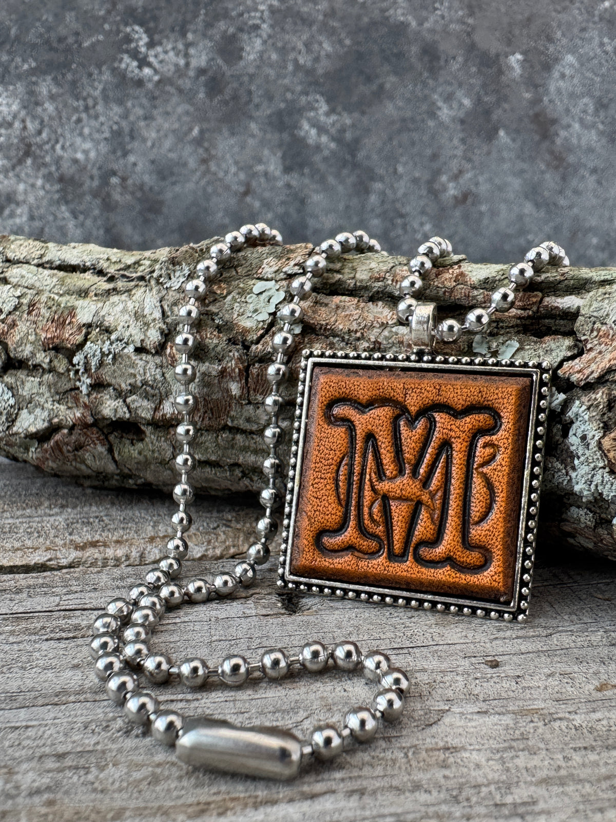 Floral Script Letter M leather initial necklace styled against natural wood