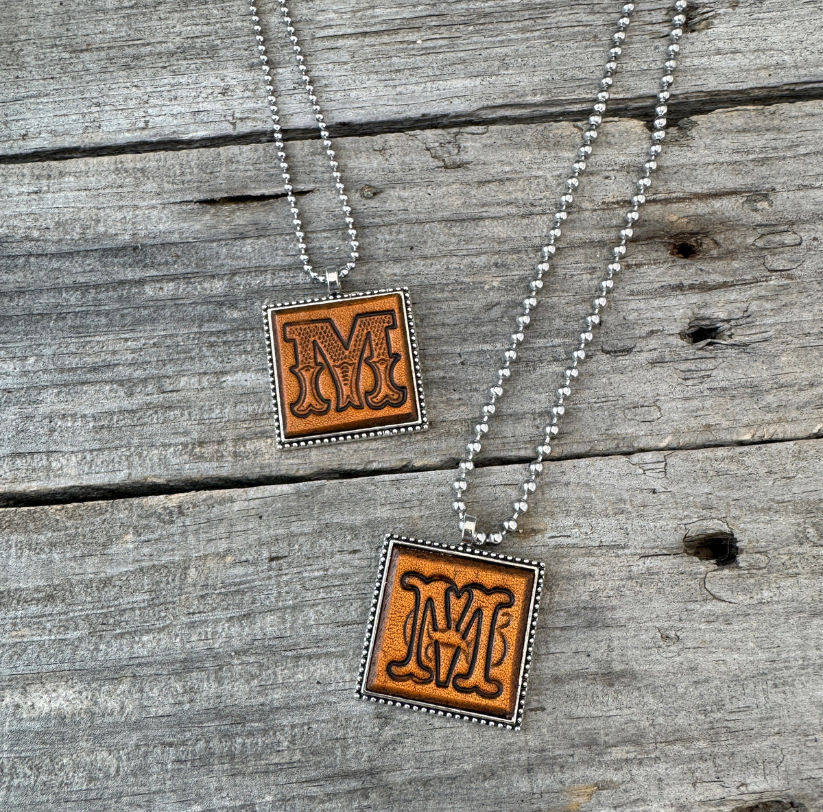 Two handmade Letter M leather initial necklaces in Western Block and Floral Script fonts