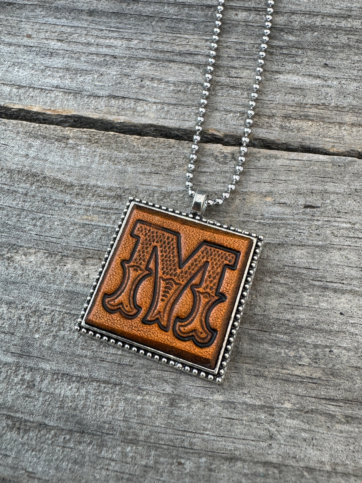 Close-up of Western Block Letter M hand-stamped leather pendant in a silver-tone square frame