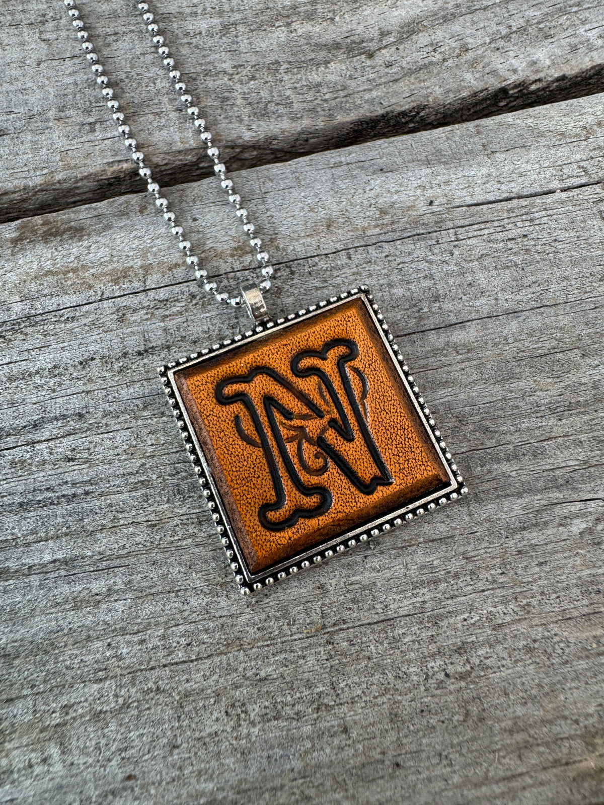 Close-up of Floral Script Letter N hand-stamped leather initial pendant with antiqued details