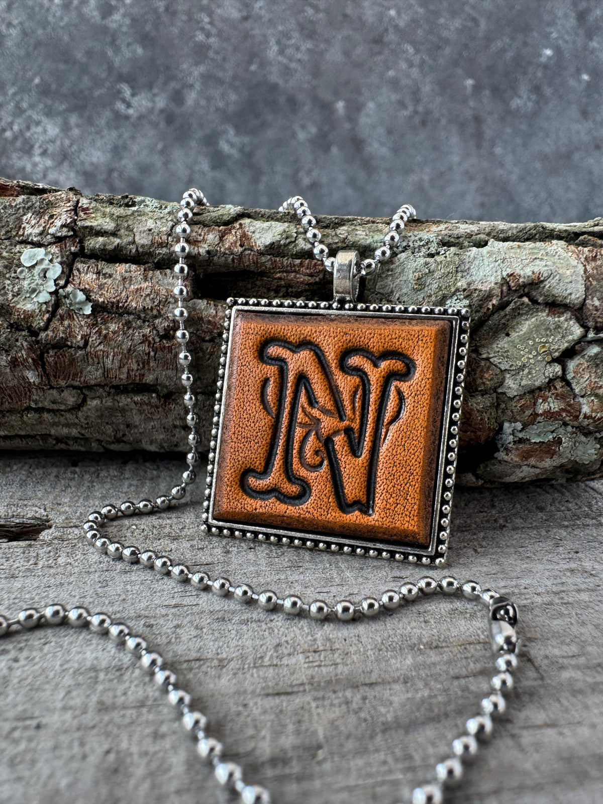 Floral Script Letter N leather initial necklace styled against natural wood