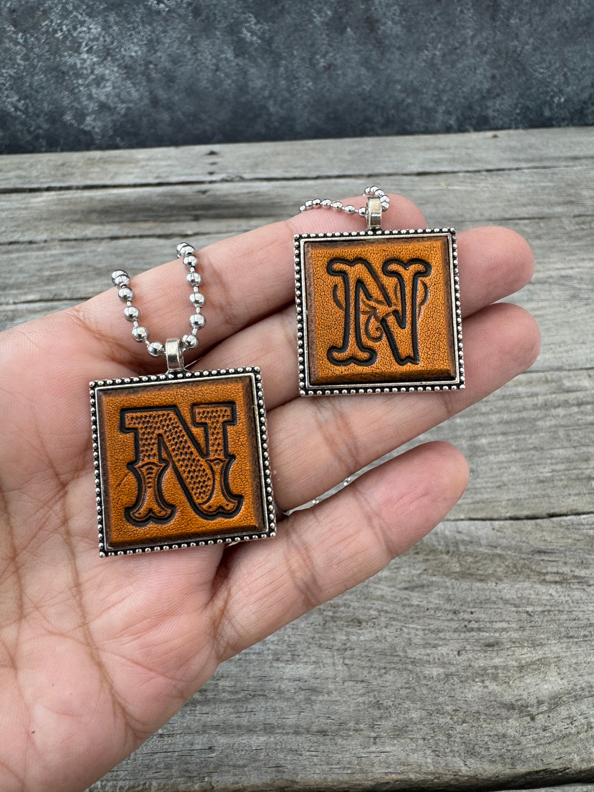 Western Block and Floral Script Letter N leather necklaces held in hand to show pendant size