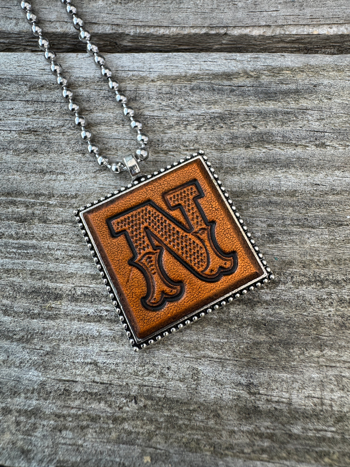 Close-up of Western Block Letter N hand-stamped leather pendant in silver-tone square frame