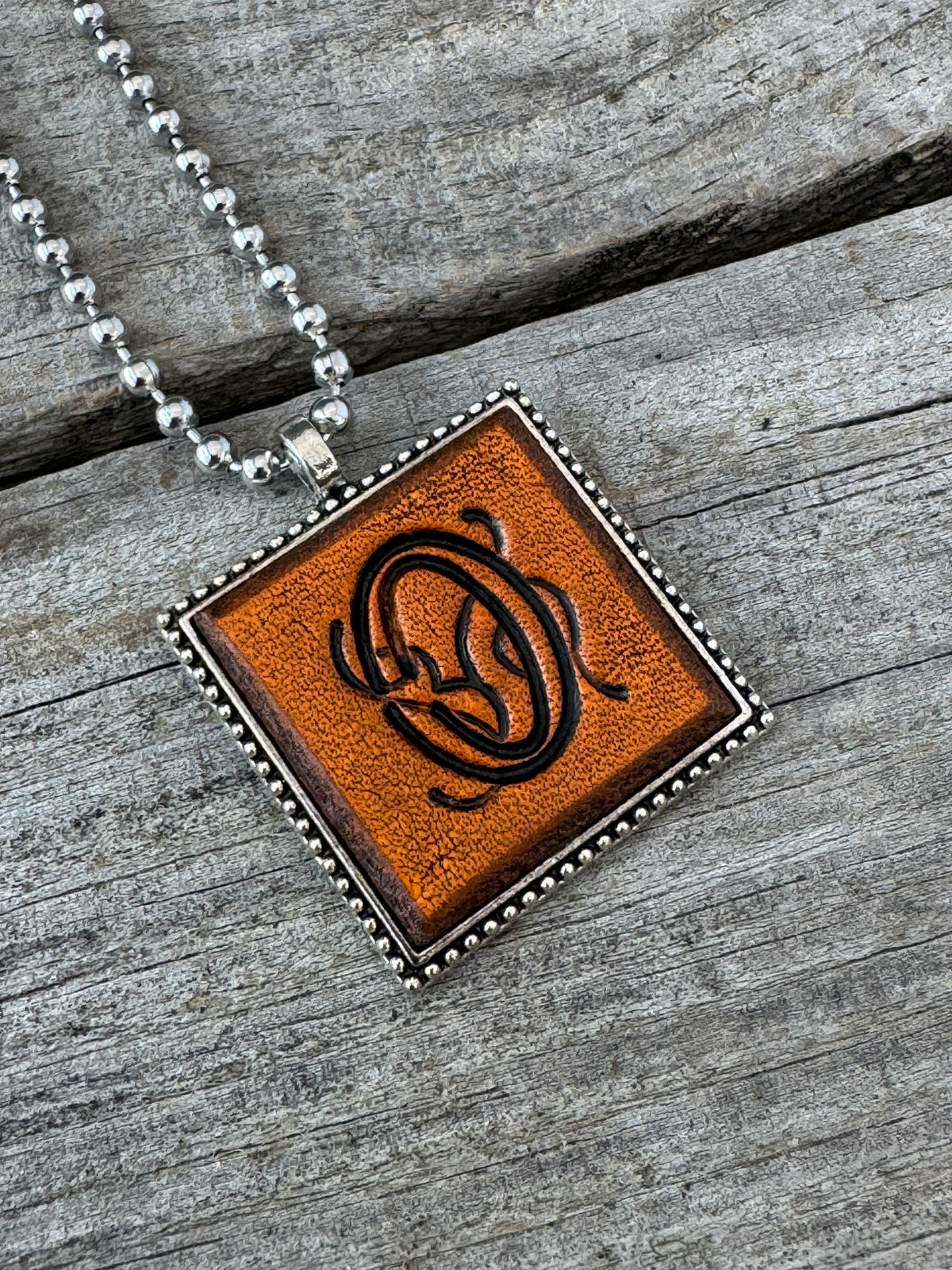 Close-up of Floral Script Letter O leather initial pendant with antiqued lettering