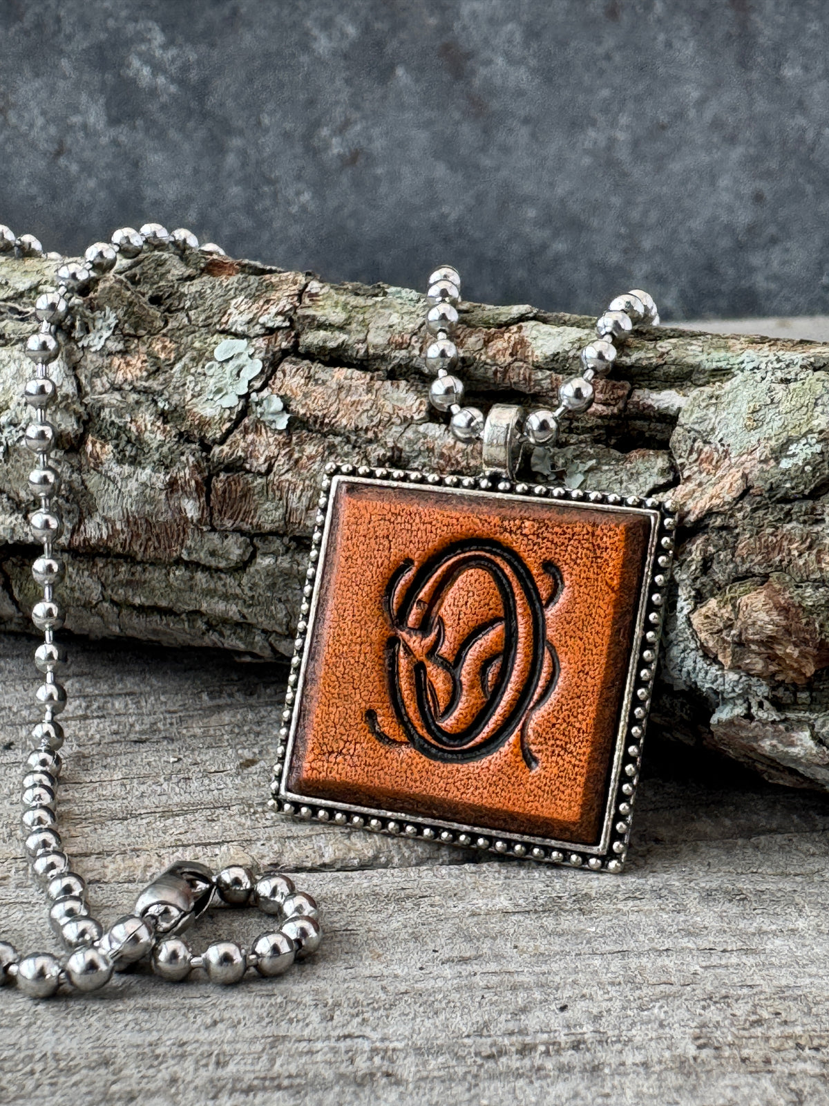 Floral Script Letter O leather initial necklace styled against natural wood