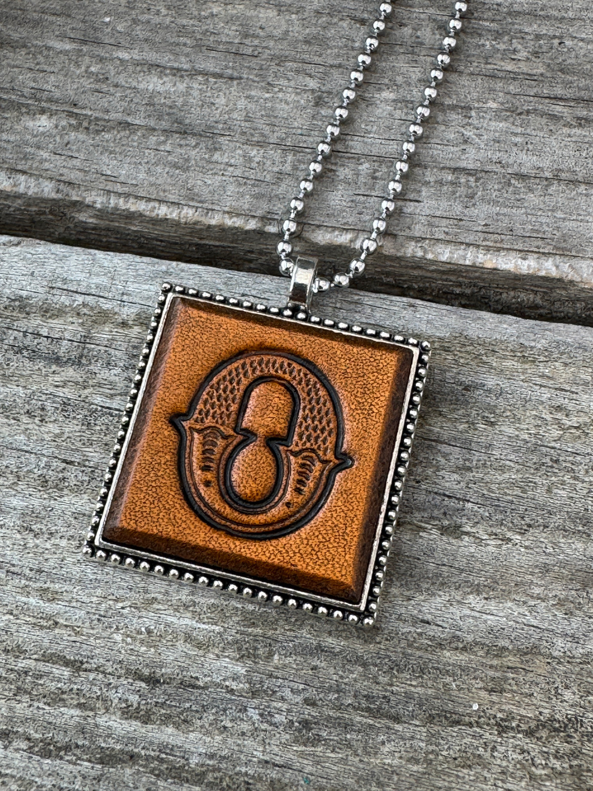 Close-up of Western Block Letter O hand-stamped leather pendant in silver-tone square frame