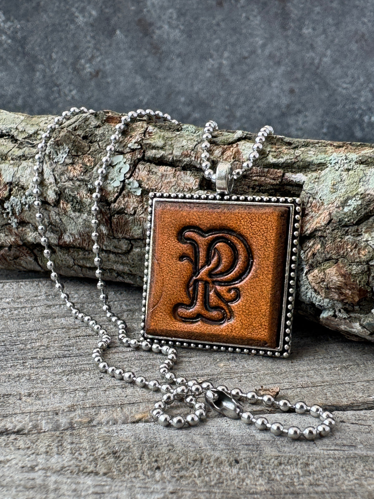 Floral Script Letter P leather initial necklace styled against natural wood