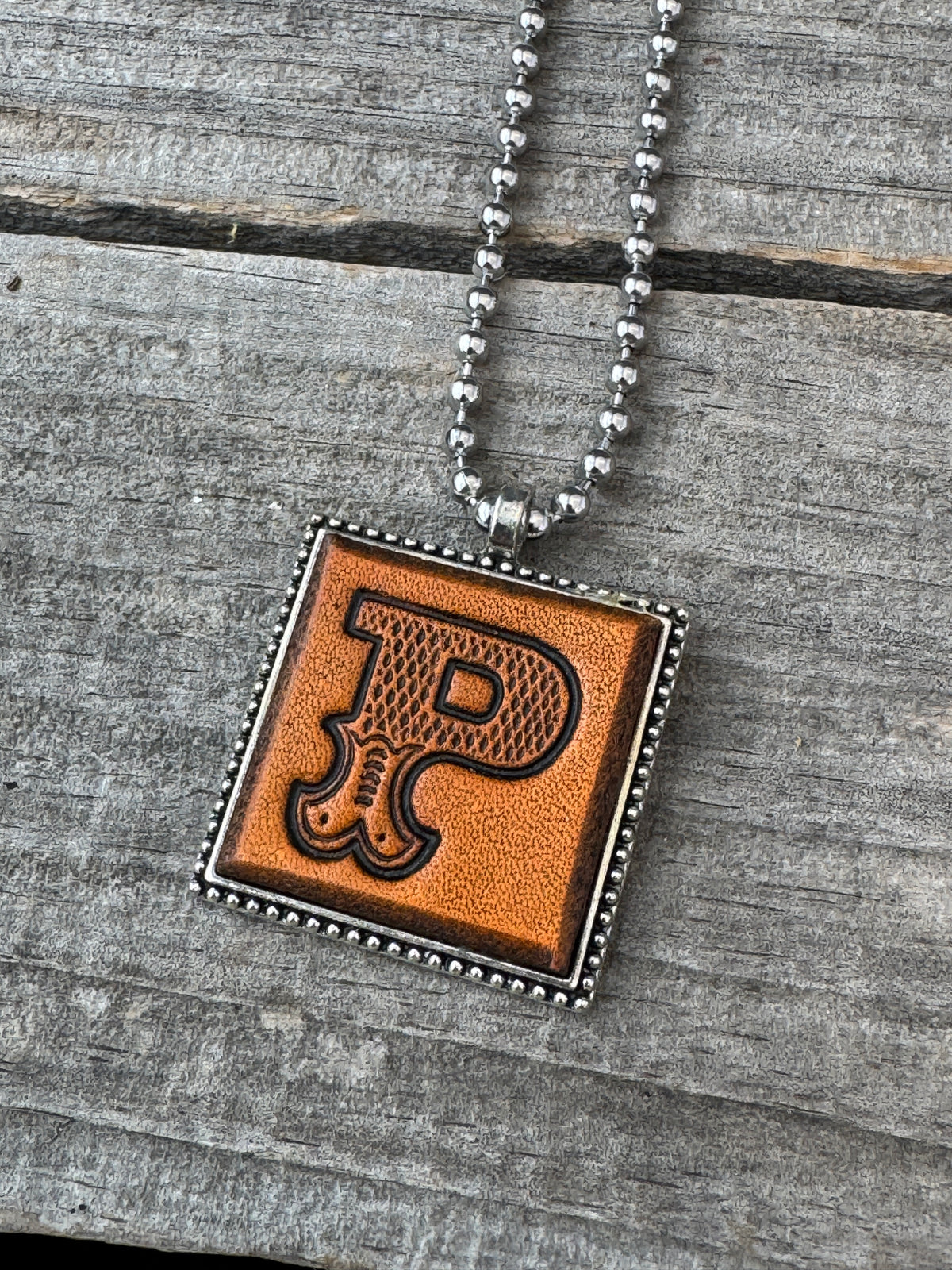 Close-up of Western Block Letter P hand-stamped leather pendant in silver-tone square frame