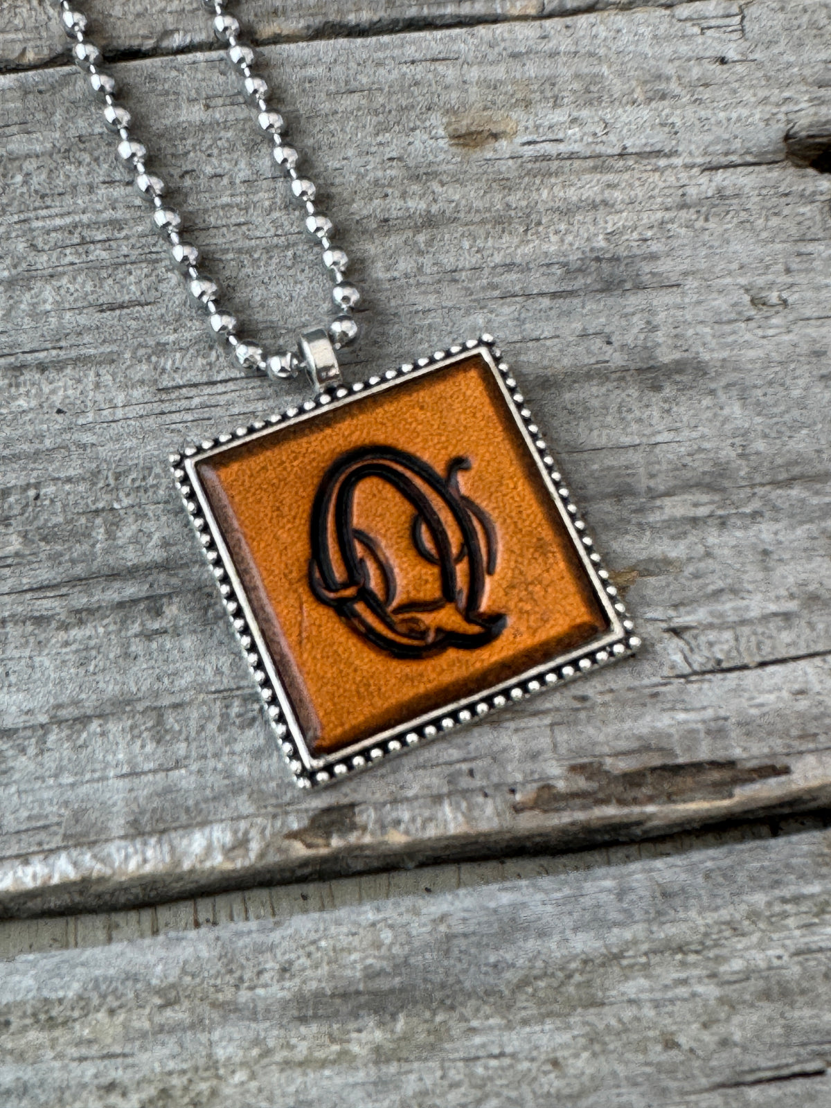 Close-up of Floral Script Letter Q leather initial pendant with antiqued lettering