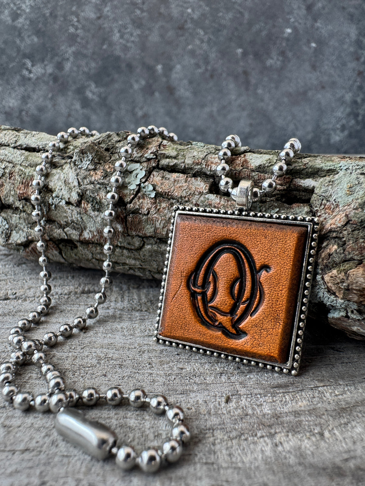 Floral Script Letter Q leather initial necklace styled against natural wood