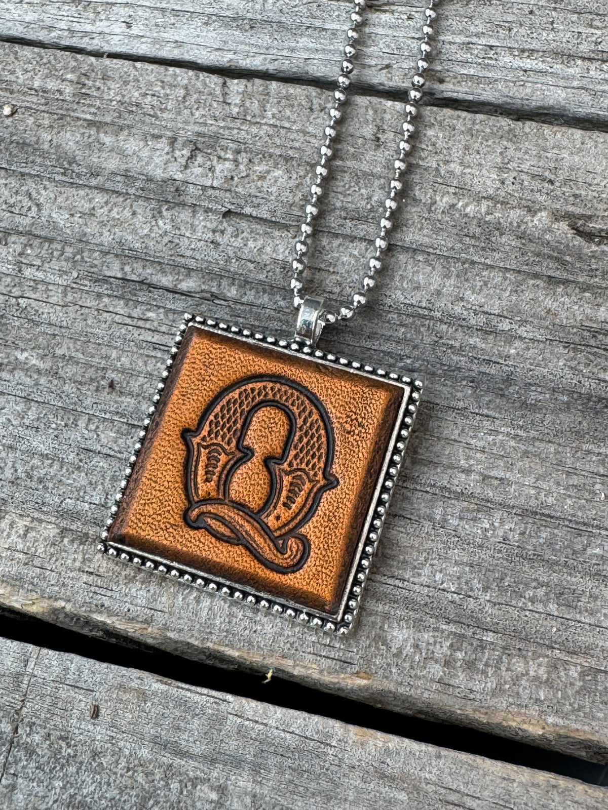Close-up of Western Block Letter Q hand-stamped leather pendant in silver-tone square frame