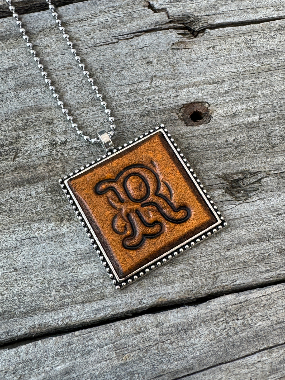 Close-up of Floral Script Letter R leather initial pendant with antiqued lettering