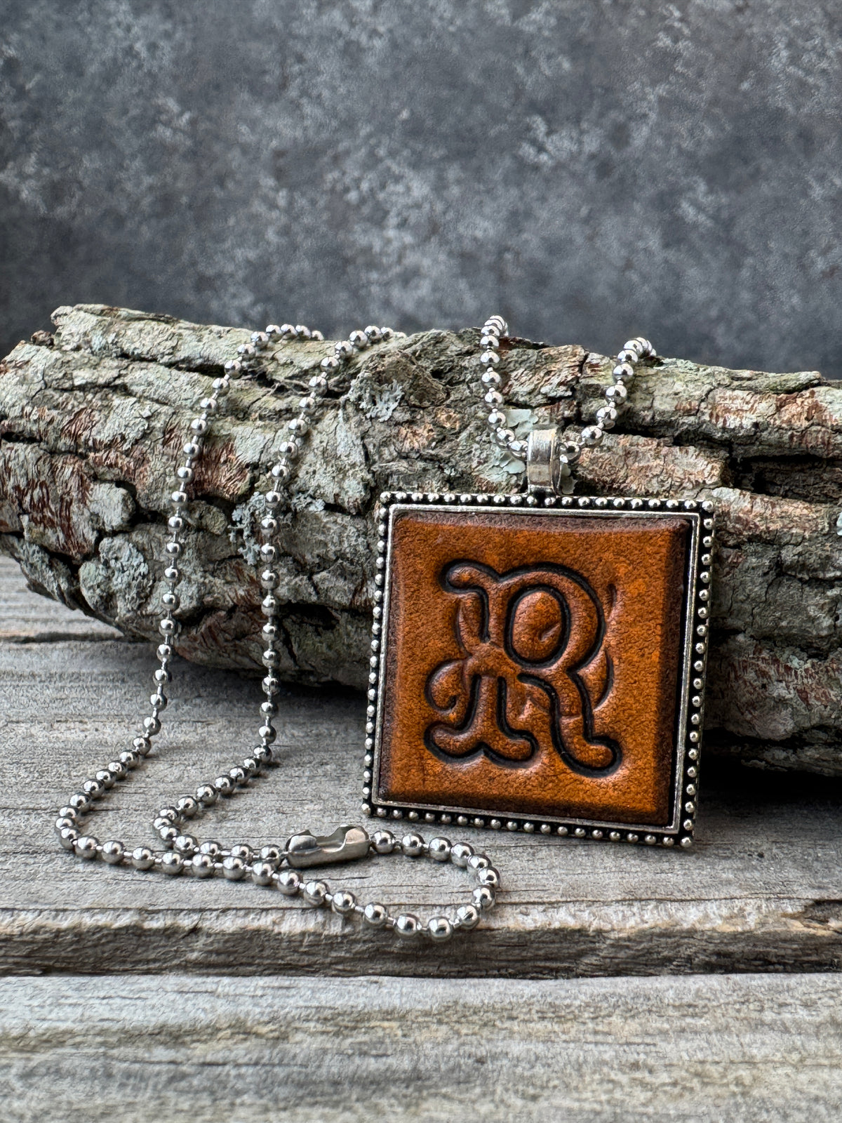 Floral Script Letter R leather initial necklace styled against natural wood