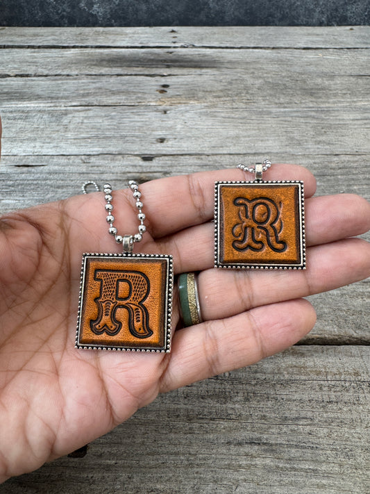 Western Block and Floral Script Letter R leather necklaces held in hand for size comparison