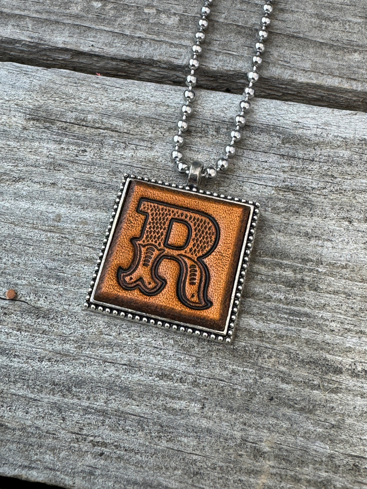 Close-up of Western Block Letter R hand-stamped leather pendant in silver-tone square frame