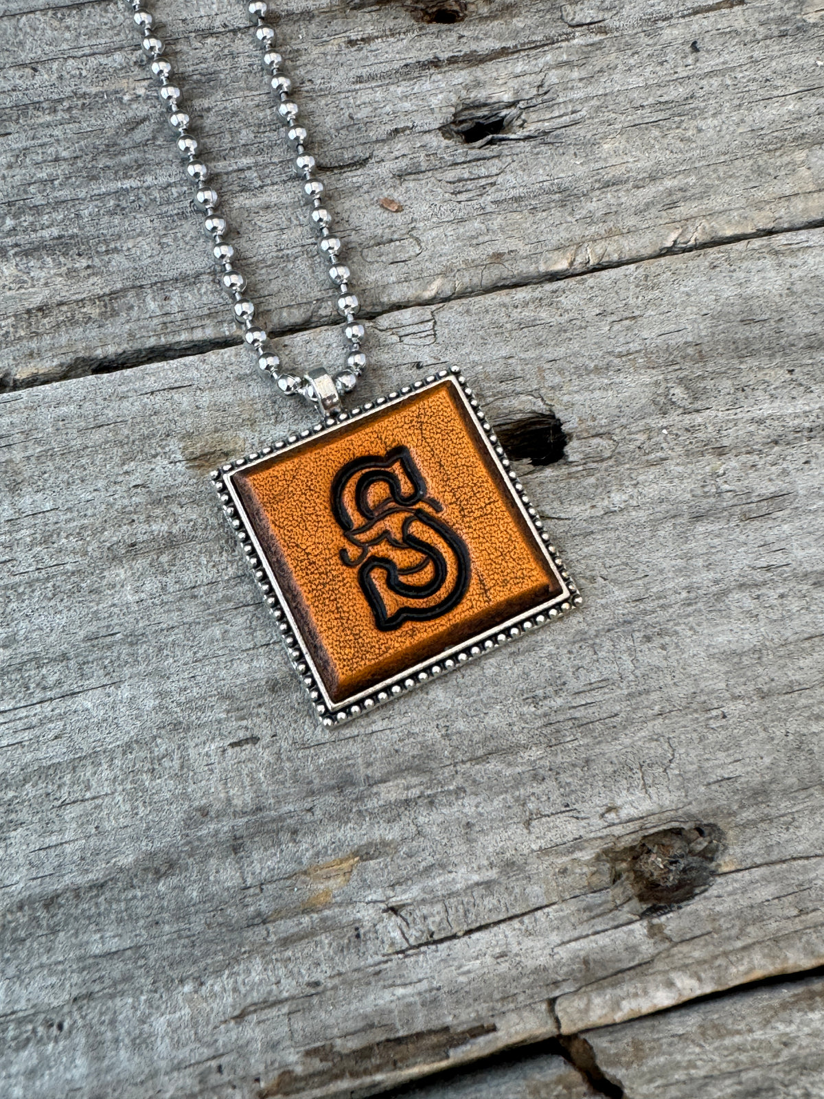 Close-up of Floral Script Letter S leather initial pendant with antiqued lettering