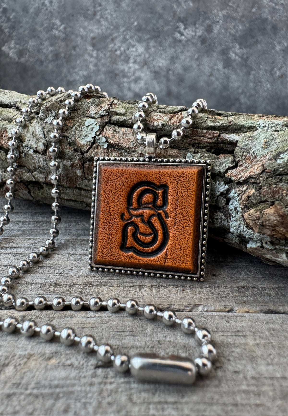 Floral Script Letter S leather initial necklace styled against natural wood