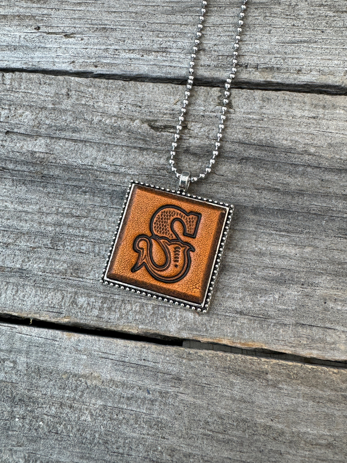 Close-up of Western Block Letter S hand-stamped leather pendant in silver-tone square frame