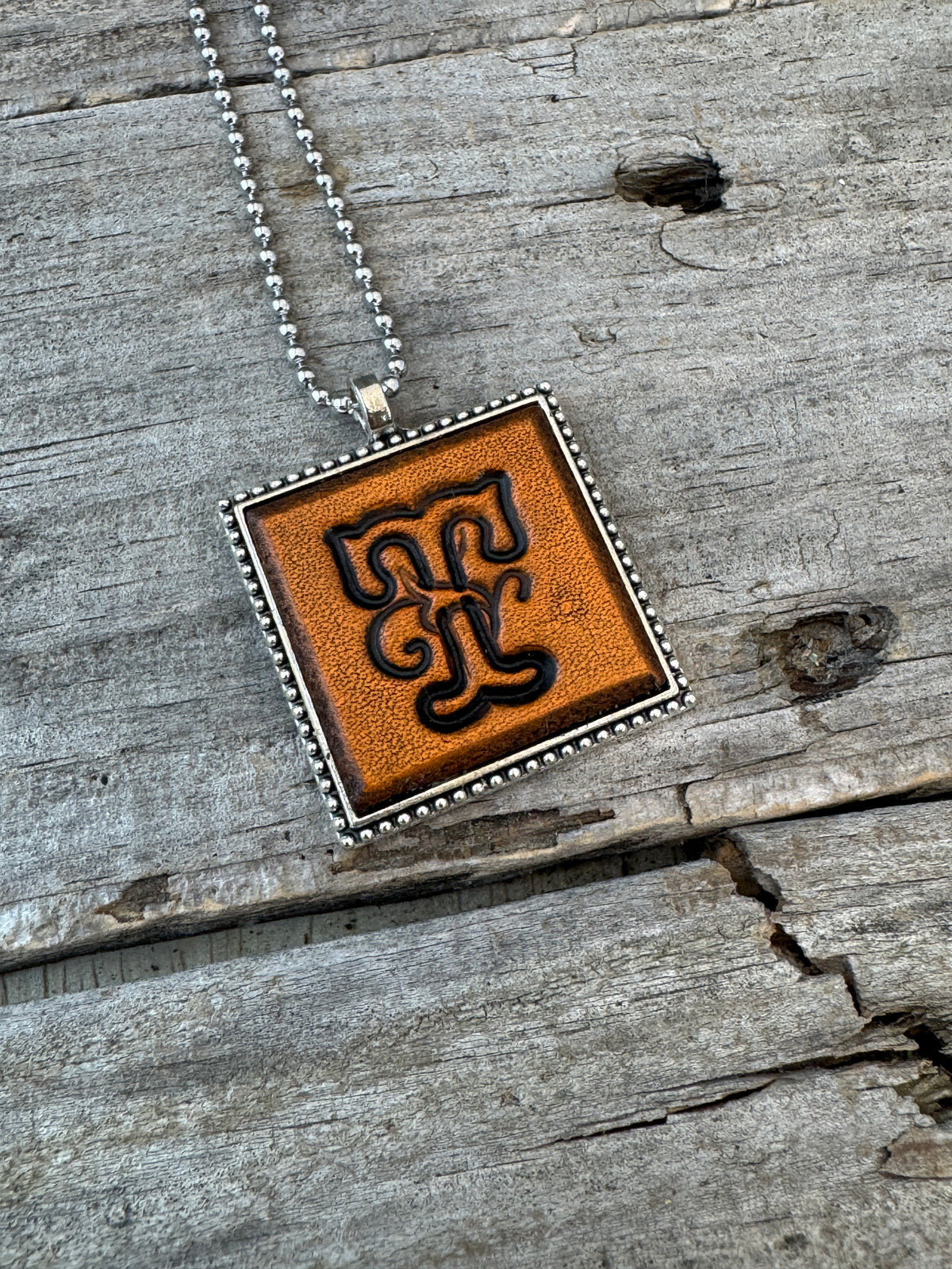 Close-up of Floral Script Letter T leather initial pendant with antiqued lettering