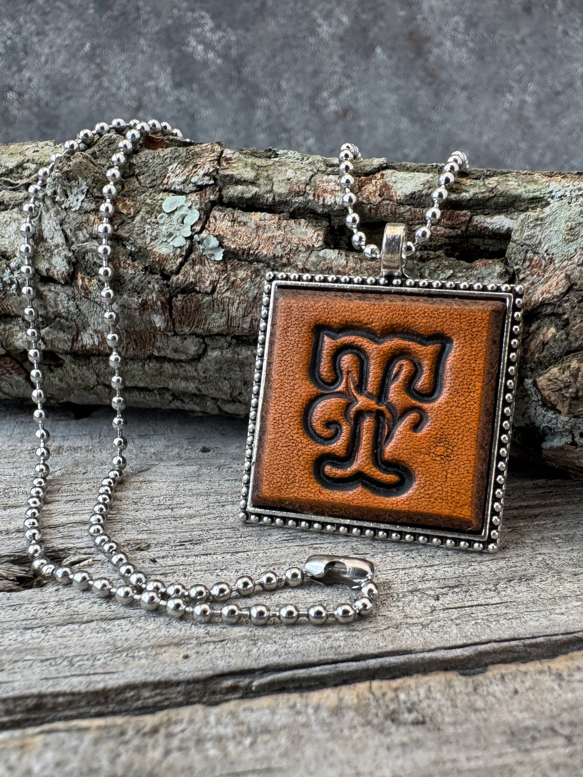 Floral Script Letter T leather initial necklace styled against natural wood