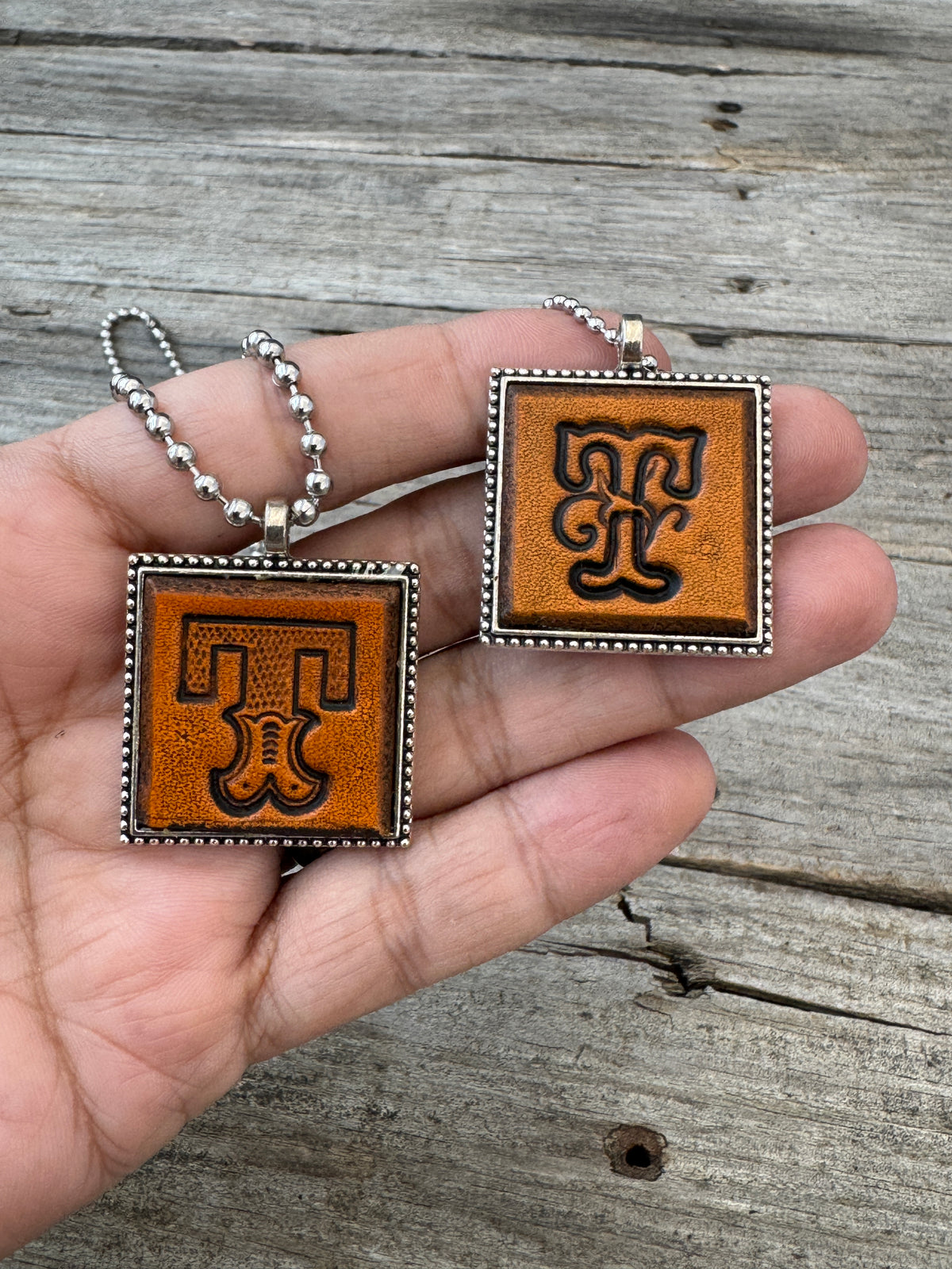 Western Block and Floral Script Letter T leather necklaces held in hand for size comparison