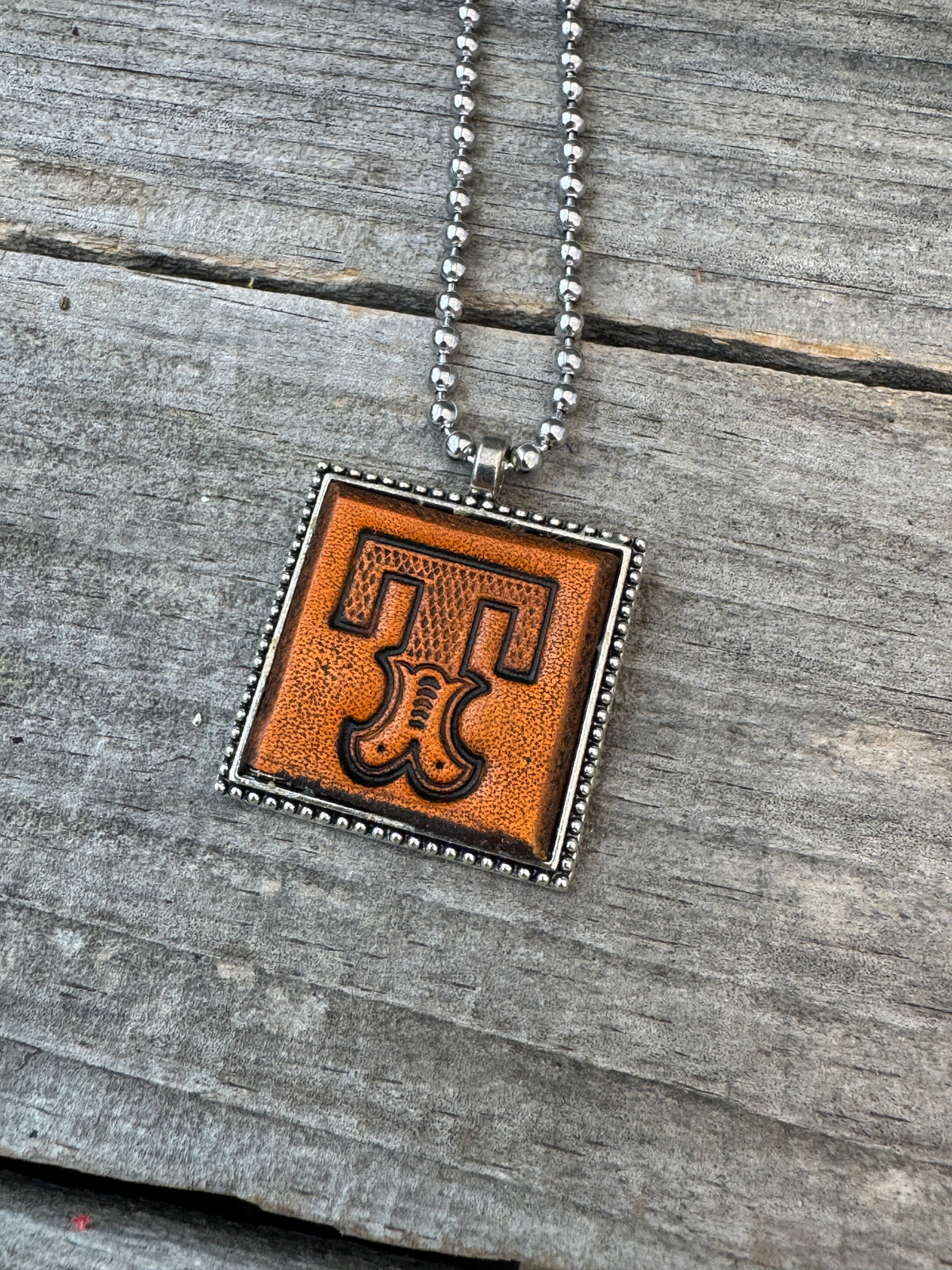 Close-up of Western Block Letter T hand-stamped leather pendant in silver-tone square frame