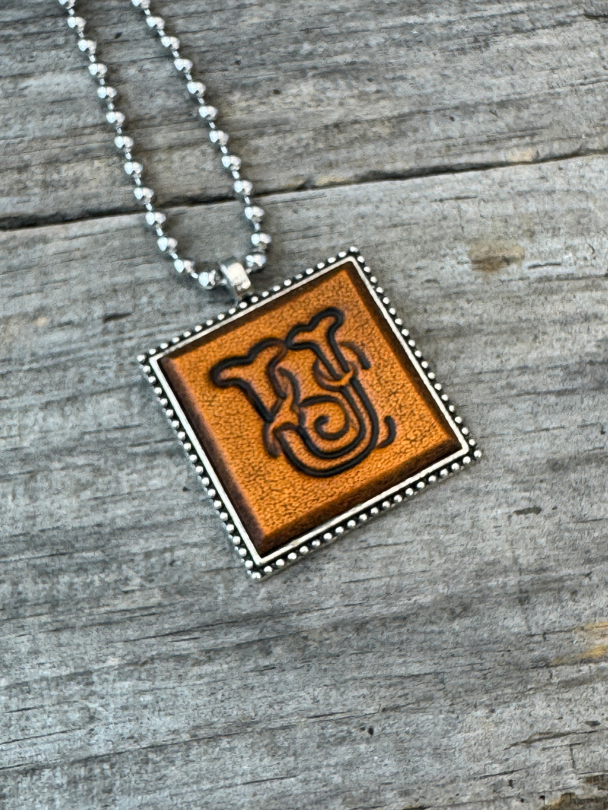 Close-up of Floral Script Letter U leather initial pendant with antiqued lettering