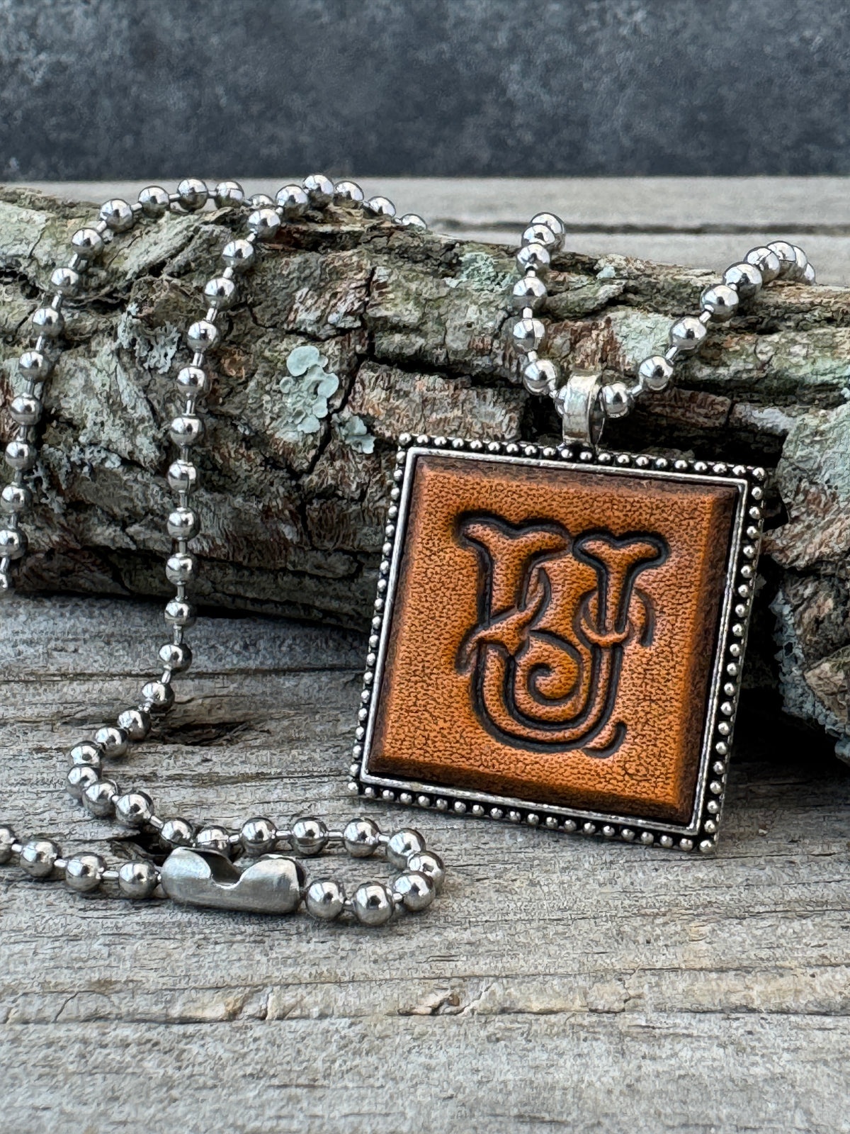 Floral Script Letter U leather initial necklace styled against natural wood