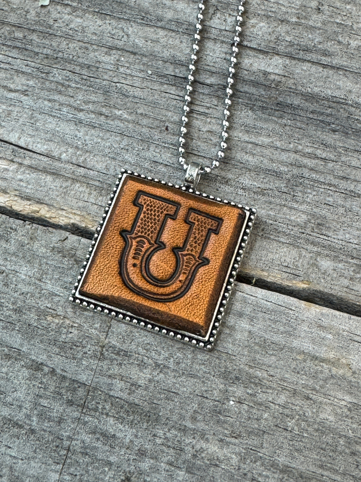 Close-up of Western Block Letter U hand-stamped leather pendant in silver-tone square frame