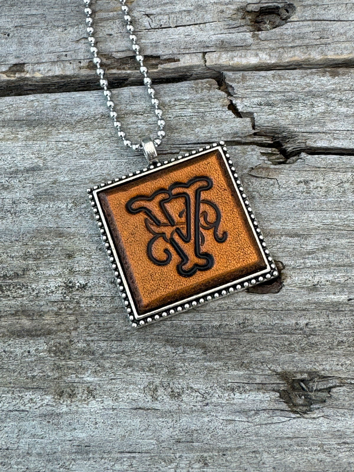 Close-up of Floral Script Letter V leather initial pendant with antiqued lettering