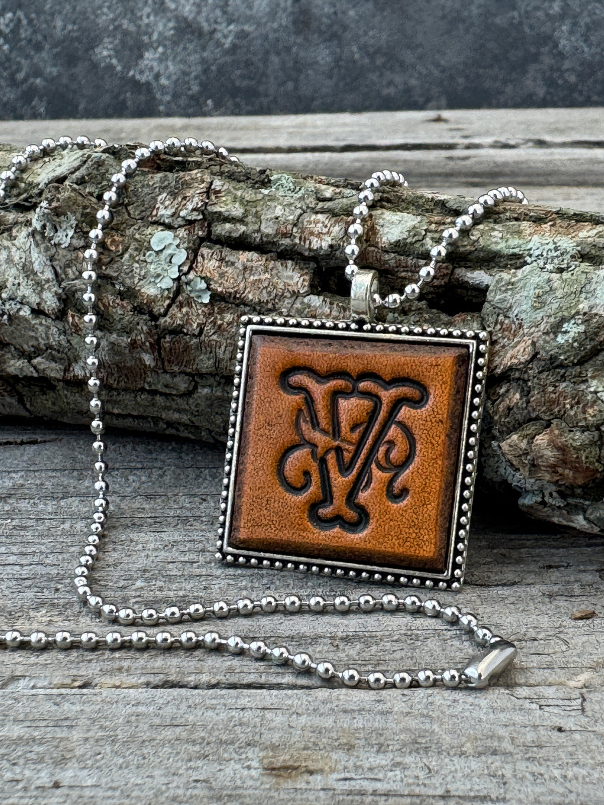 Floral Script Letter V leather initial necklace styled against natural wood