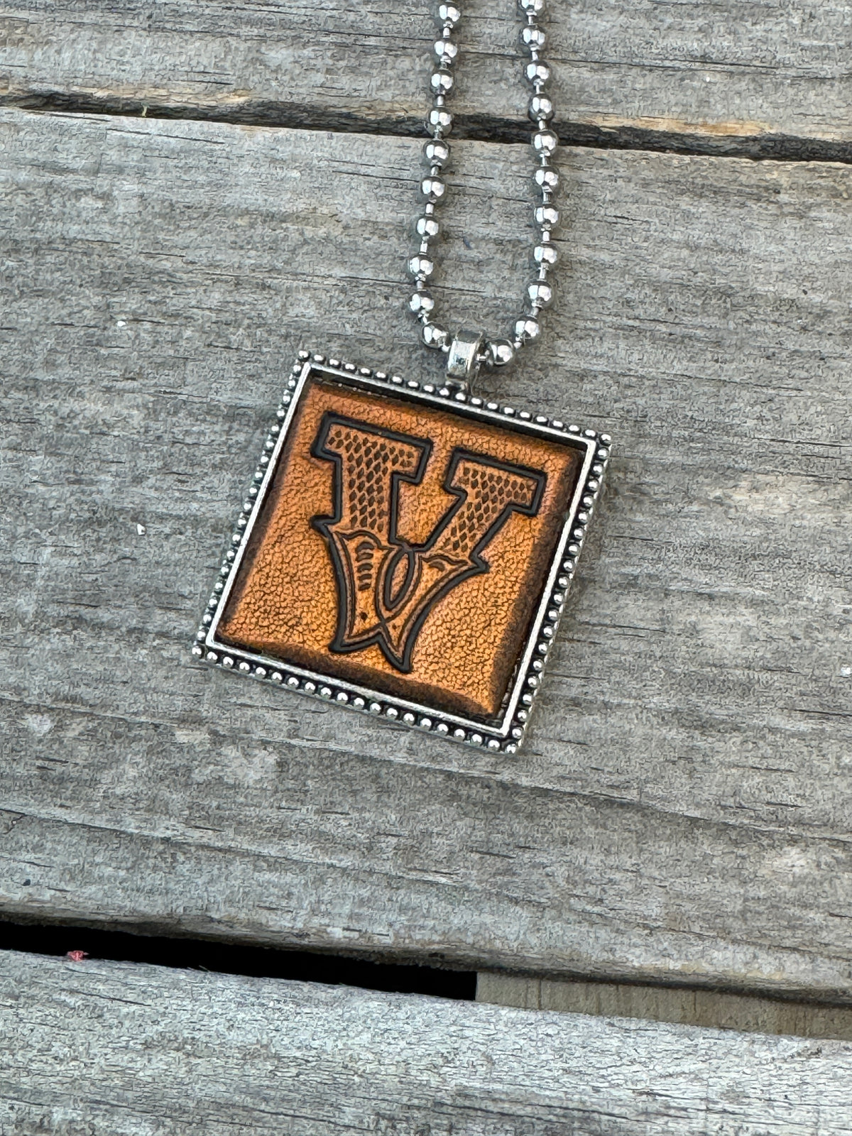 Close-up of Western Block Letter V hand-stamped leather pendant in silver-tone square frame