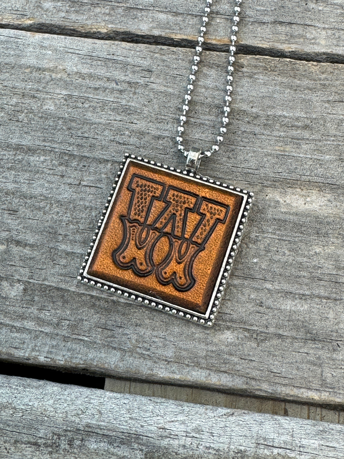 Close-up of Western Block Letter W hand-stamped leather pendant in silver-tone square frame