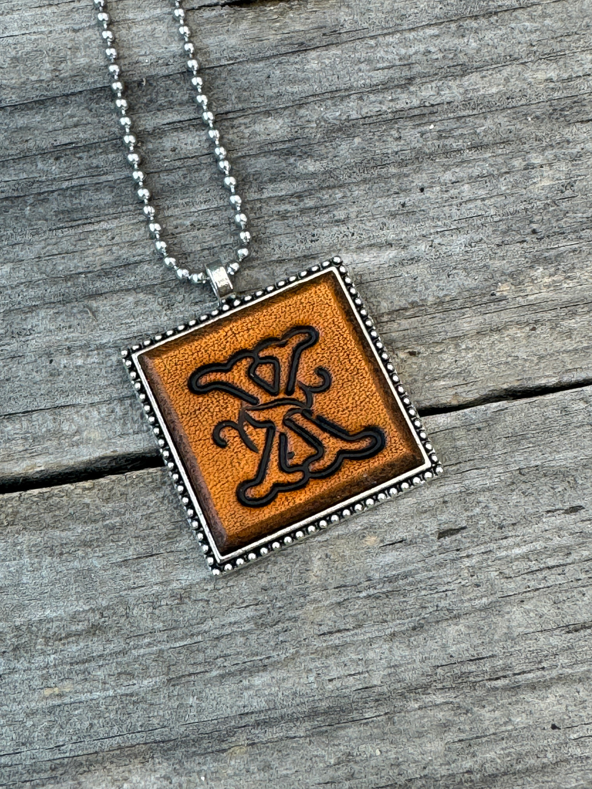 Close-up of Floral Script Letter X leather initial pendant with antiqued lettering