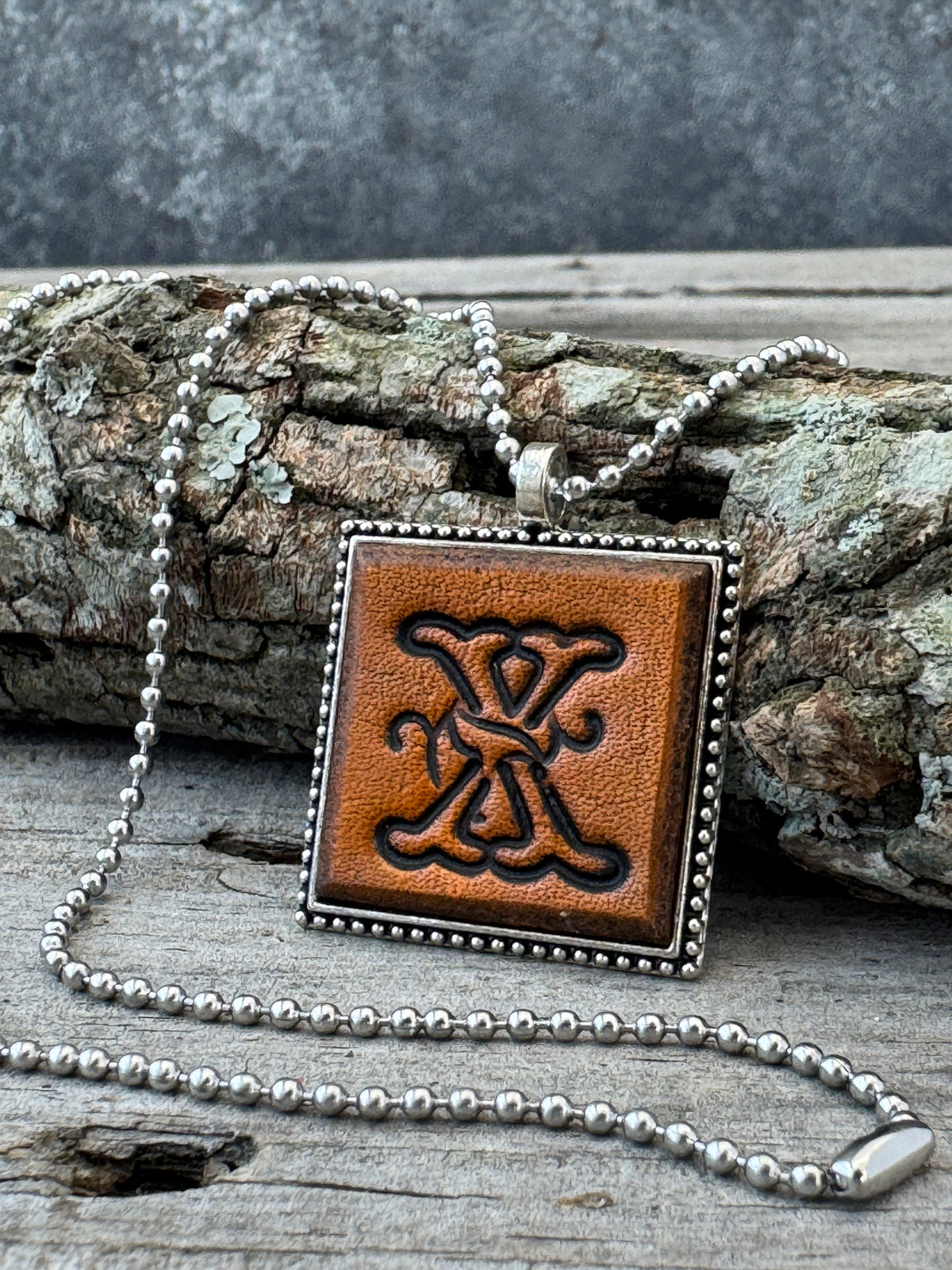 Floral Script Letter X leather initial necklace styled against natural wood