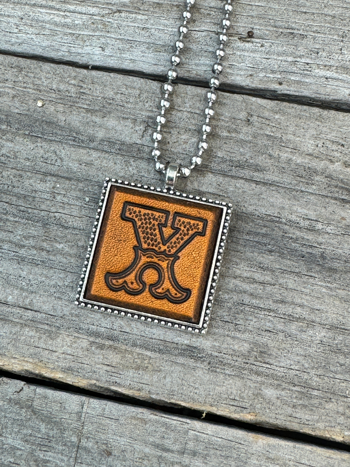 Close-up of Western Block Letter X hand-stamped leather pendant in silver-tone square frame